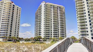 A high-rise residential building with multiple balconies, a wooden boardwalk, and a clear blue sky. - Fabulous condo, excellent reviews!! 2 chairs and 1 umbrella (Available Mar-Oct) (Navarre)