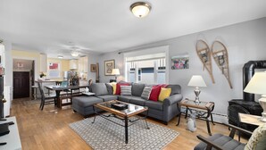 A living room with a grey sofa, coffee table, and a dining area with a table and chairs. - Dog Friendly with Hot Tub - Alpine Adventure (Red Lodge)