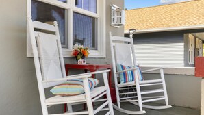 Two white rocking chairs with striped pillows on a balcony with a red table and a vase of flowers. - Dog Friendly with Hot Tub - Alpine Adventure (Red Lodge)