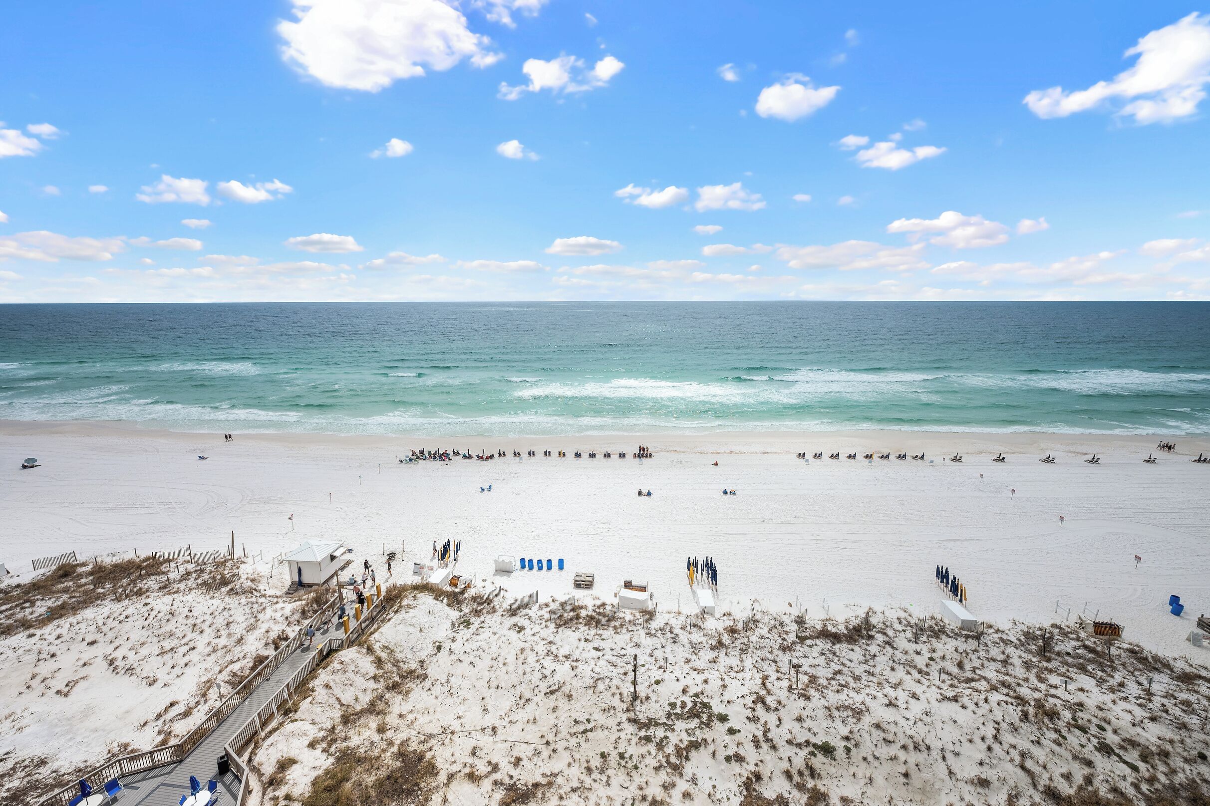 A beach with a clear sky, sandy shore, and a wooden boardwalk leading to the water.