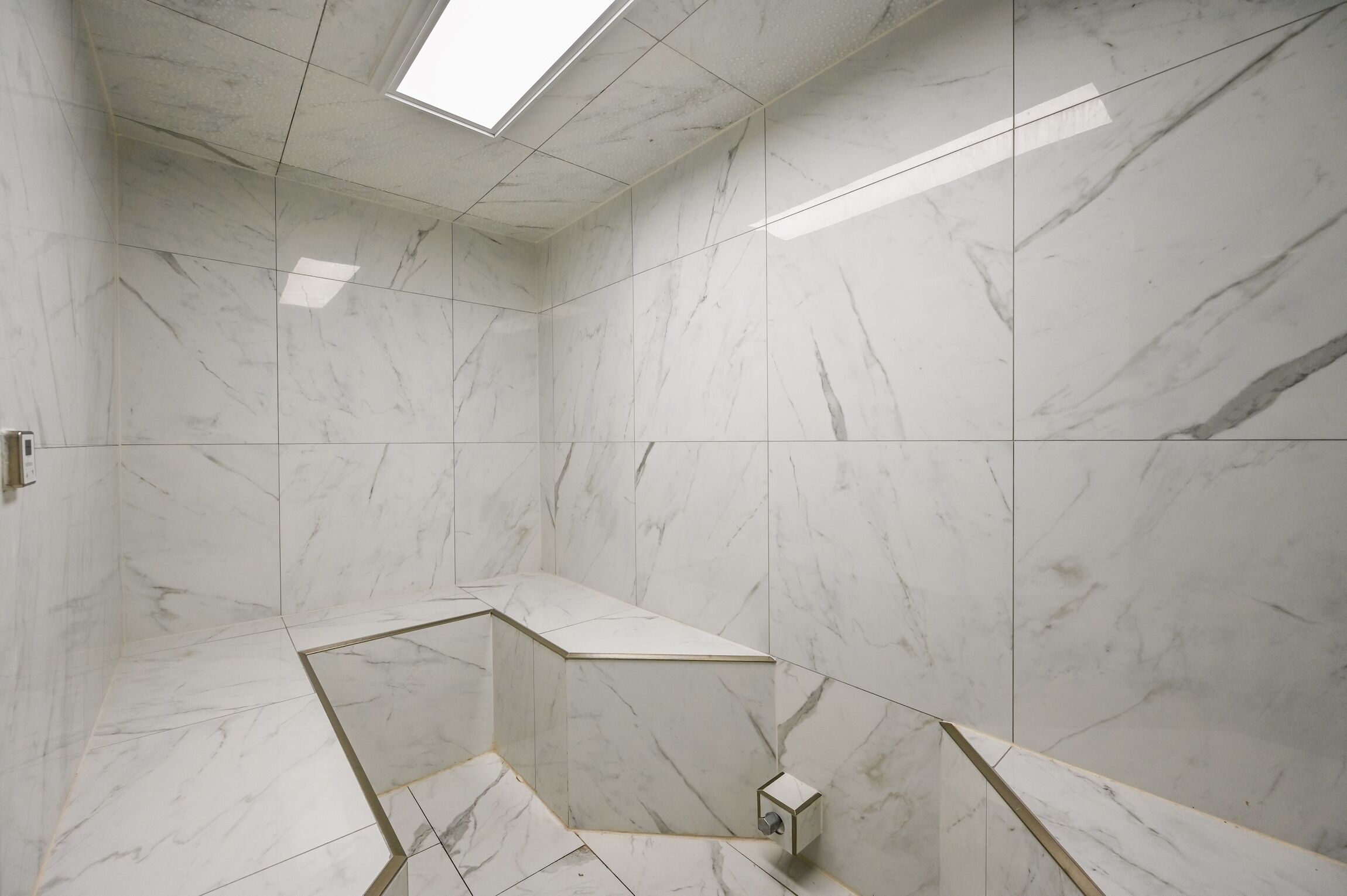 A modern bathroom with white marble tiles, a skylight, and a built-in shower area.