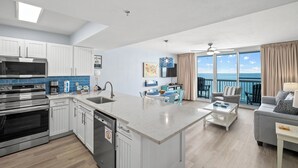 A modern kitchen with built-in appliances, a dining area with a view, and a living room with a balcony overlooking the ocean.