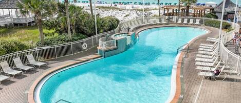 Uma piscina com design curvo, rodeada por espreguiçadeiras e um deck.