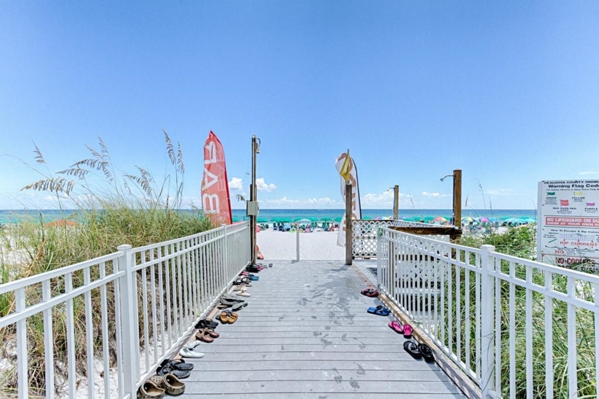 Ein Holzsteg führt zu einem Strand, an dem ein Schild darauf hinweist, dass keine Rettungsschwimmer Dienst haben.