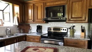 A kitchen with wooden cabinets, a stainless steel stove, a microwave, and granite countertops.