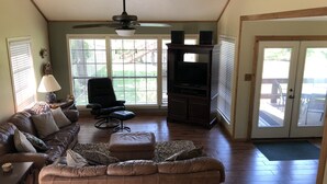 A living room with a brown leather sofa, a black armchair, a wooden entertainment center, and a ceiling fan.