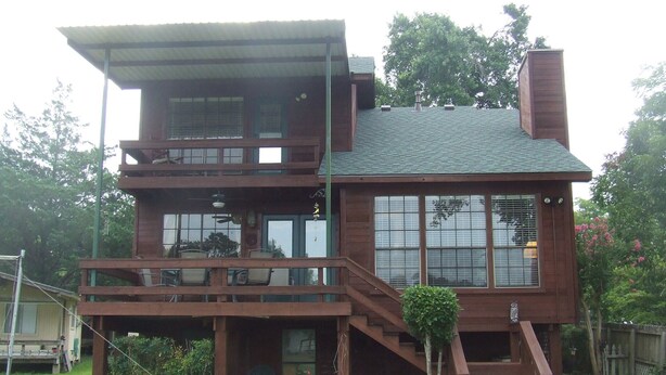 A two-story wooden house with a balcony, a chimney, and a small garden area.