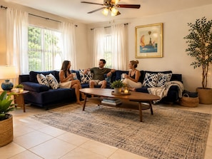 A living room with a dark blue sofa, a coffee table, and a large window with curtains. - Mid-Century Retreat close to Everything. (Sarasota)