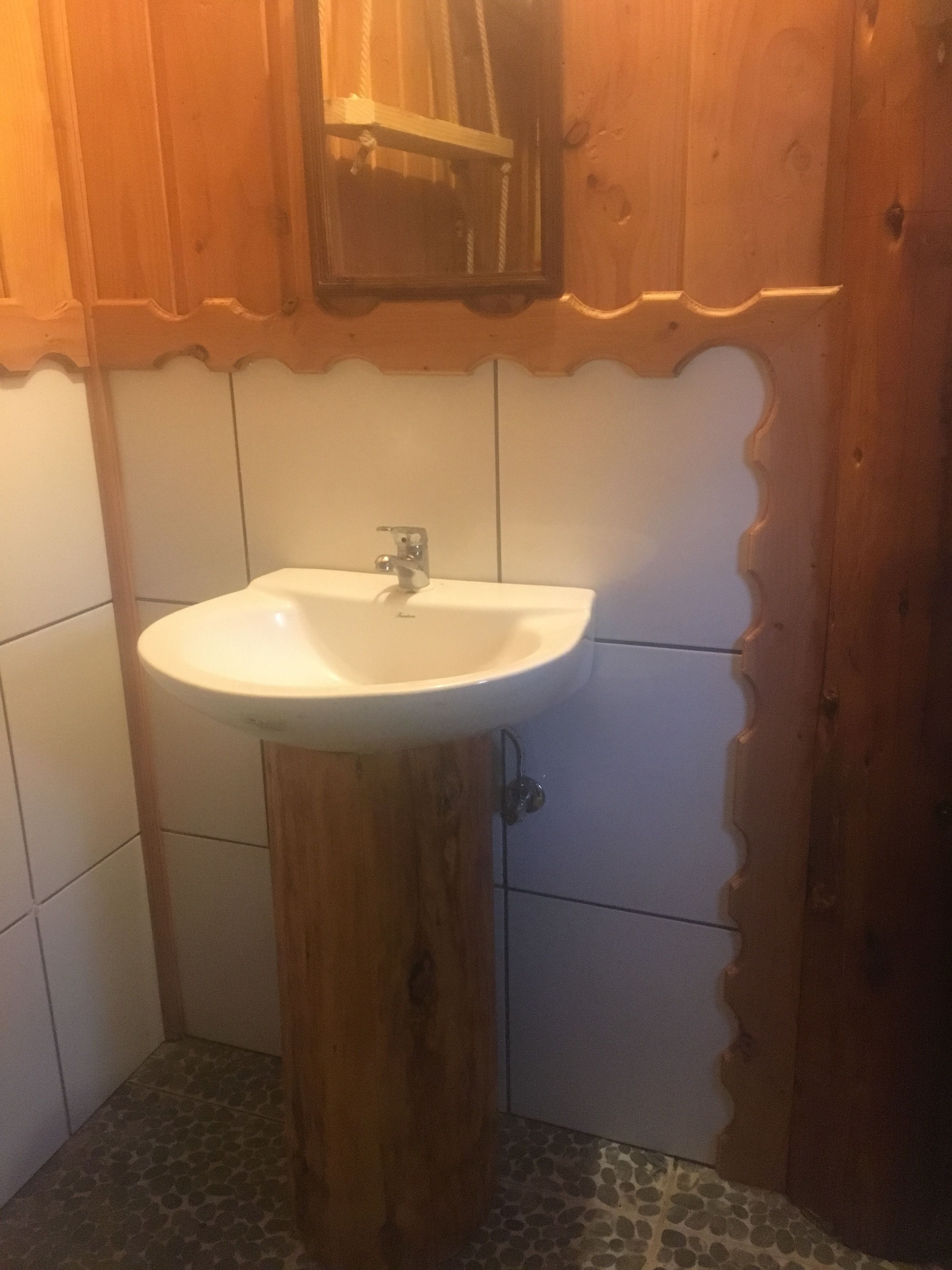 A bathroom with a wooden vanity, white tiles, and a white sink.