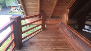 Eine Holzterrasse mit roter Geländer, die zu einem Blockhaus-Innenraum führt.