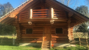 Eine Blockhütte mit Balkon, einer Haustür und einem kleinen Fenster an der Seite.