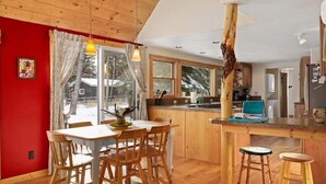 Un intérieur chaleureux, avec des murs en bois, comprenant un coin repas, une cuisine et de grandes fenêtres.