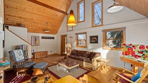 Un salon spacieux avec un haut plafond en bois, un grand canapé, une table basse et une bibliothèque.