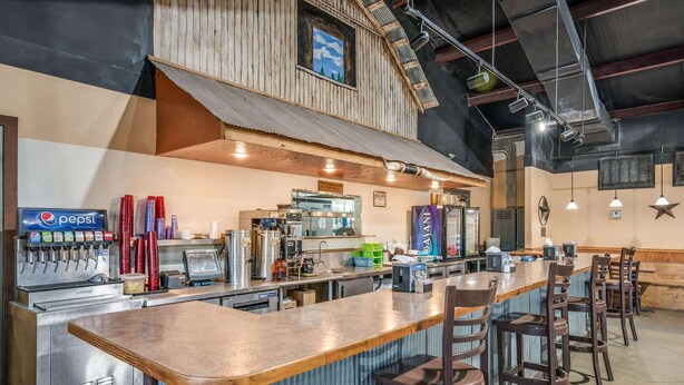 A bar area with a long counter, stools, a Pepsi machine, and a kitchen in the background. - Rodeway Inn Gurdon I-30 (Gurdon)