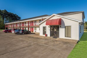 A motel with a red awning, multiple floors, and a parking lot with several cars.
