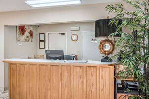 Balcão de recepção com acabamento em madeira, um relógio, certificados emoldurados e uma placa de acesso privativo.