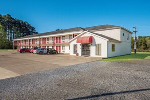 A motel with a two-story structure, a red awning, and a parking lot with several cars.