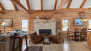Cozy cabin interior with a stone fireplace, comfortable seating area, and large window offering a view of the outdoors.