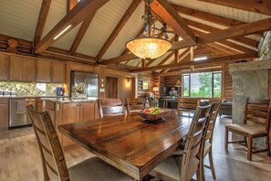 A spacious kitchen with wooden beams, a large dining table, and a stone fireplace. - Grizzly Peak Cabin (Red Lodge)