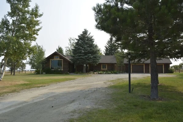A rustic log cabin with a gravel driveway and surrounding trees.