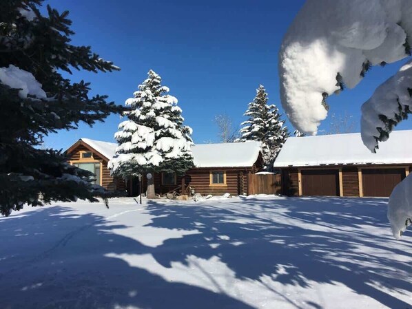 A snow-covered lodge with a wooden exterior, large windows, and a garage.