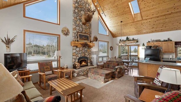 A spacious living area with a stone fireplace, wooden furniture, and large windows.