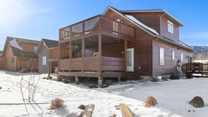 A wooden cabin with a balcony, a covered porch, and a snow-covered ground. - Mountain View Tee and Ski (Red Lodge)