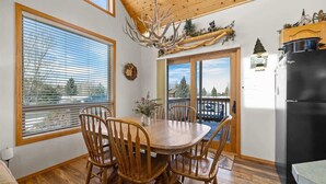 A dining area with a wooden table and chairs, a chandelier, and a view through the window. - Mountain View Tee and Ski (Red Lodge)