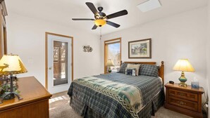 A bedroom with a bed, nightstands, a desk, a ceiling fan, and a door. - Mountain View Tee and Ski (Red Lodge)