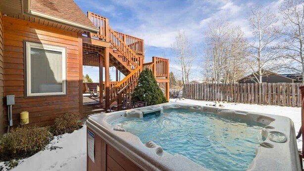 A wooden house with a hot tub, a wooden staircase, and a snow-covered yard. - Mountain View Tee and Ski (Red Lodge)