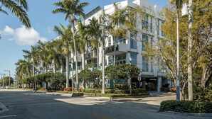 Un edificio moderno de varios pisos, rodeado de palmeras y vegetación.