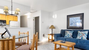 Un salon moderne avec un canapé bleu, des chaises en bois, une table à manger en verre et une table basse.