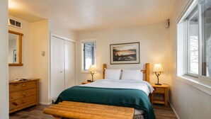 Une chambre à coucher avec un lit, des lampes de chevet, un banc en bois, une commode et un tableau au mur.