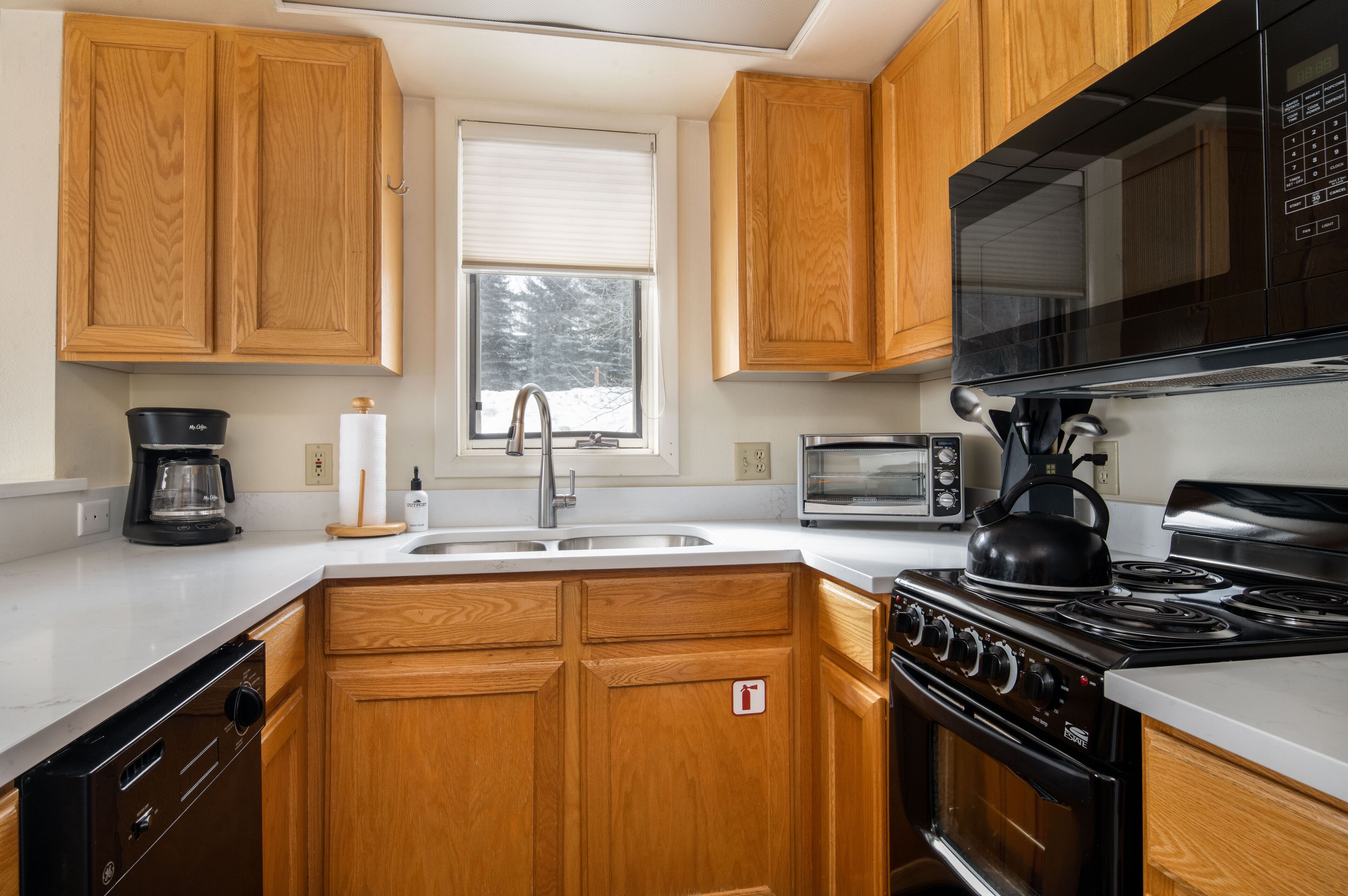 A kitchen with wooden cabinets, a black stove, a microwave, and a coffee maker.
