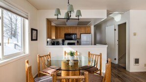 Une cuisine moderne avec des meubles en bois, une table à manger en verre et un luminaire suspendu.