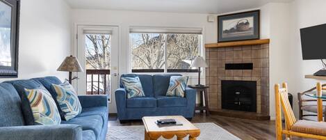 A living room with a blue sofa, a small wooden coffee table, a fireplace, and a television.