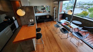 Un appartement moderne doté d’une cuisine, d’un coin repas et d’une grande fenêtre donnant sur un paysage urbain.