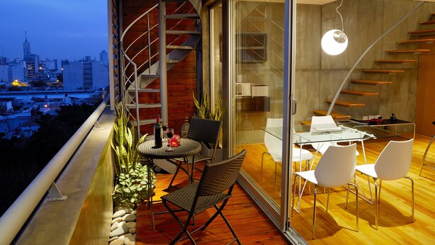 Un espace de repas moderne avec une table et des chaises en verre, un escalier en colimaçon et une vue sur la ville.
