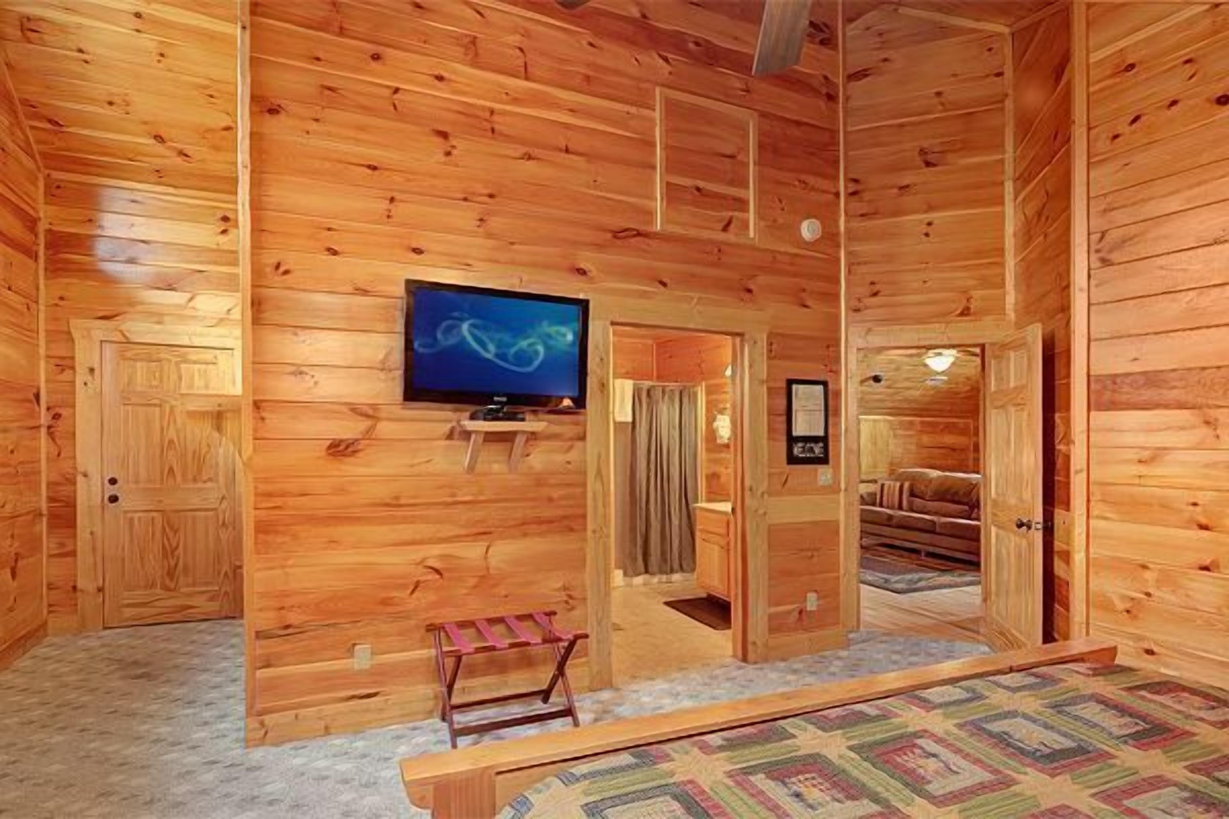 A wooden cabin interior with a television, a bench, and a door leading to another room.