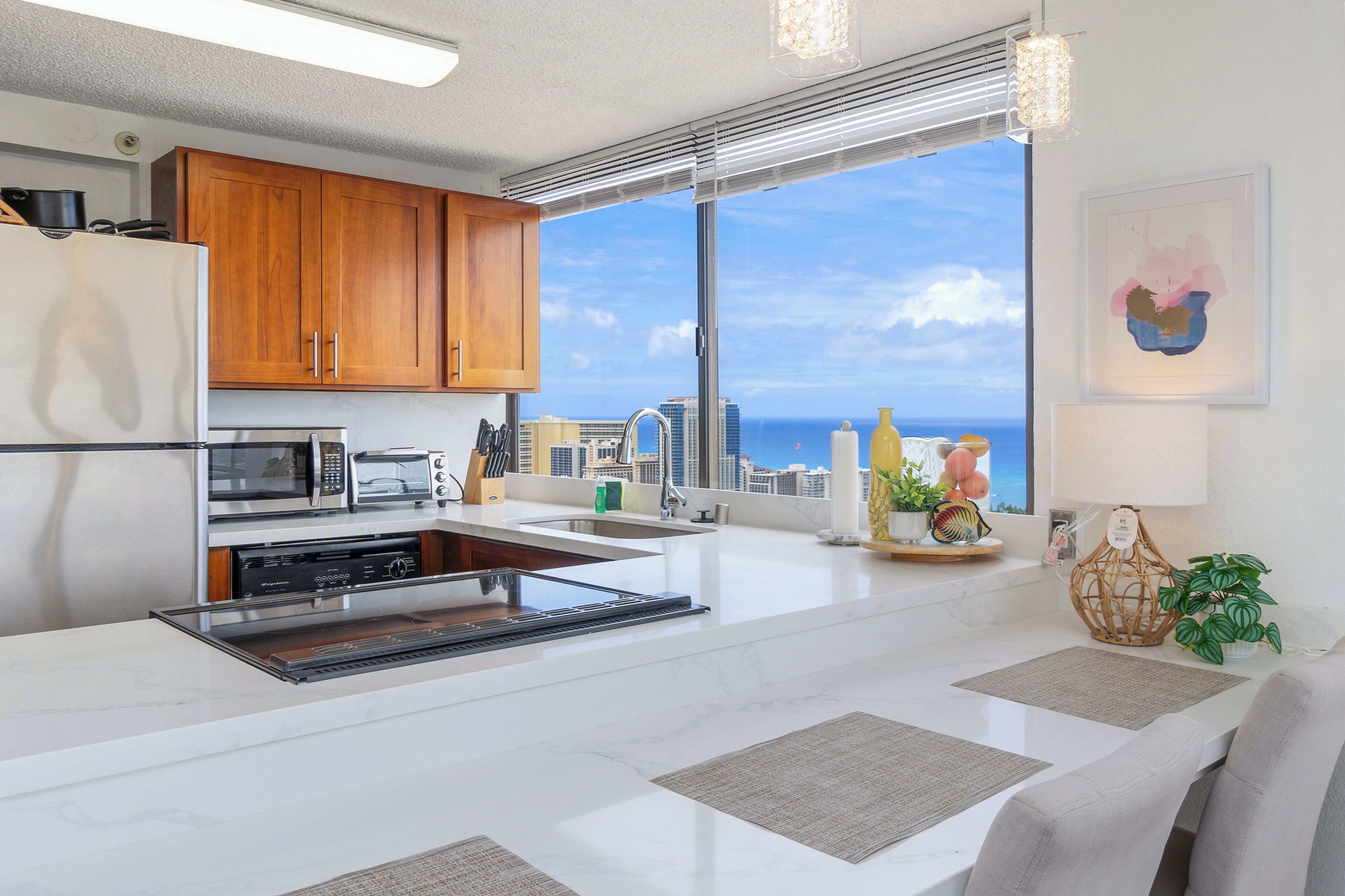 A modern kitchen with wooden cabinets, stainless steel appliances, and a large window offering a view of the city and ocean.
