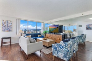 A modern living room with a city view, a large flat-screen TV, and a dining area with a wooden cabinet. - 2bed/2bath Penthouse Ocean View...Recent Luxurious Renovation (Honolulu)