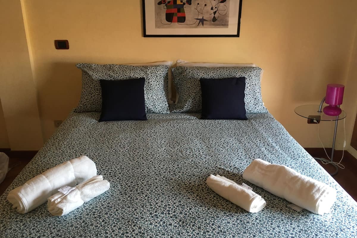A bed with a patterned bedspread, two pillows, and two rolled towels.