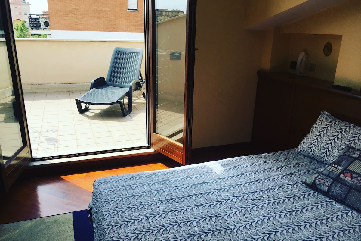 A hotel room with a bed, a chair, and a view of the outside.