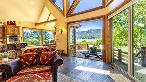 A spacious living area with a view of a lake and mountains, a dining area with a table and chairs, and a kitchen with modern appliances.