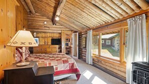 A log cabin bedroom with a bed, a lamp, a TV, and large windows. - Rendezvous Lodge (Red Lodge)