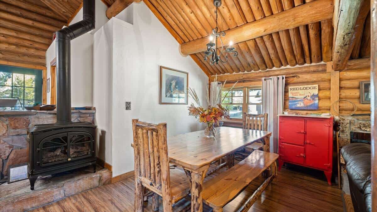 A rustic cabin interior with a stone fireplace, wooden dining table, and a red cabinet.