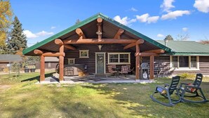 A log cabin with a covered porch, outdoor seating, and a well-maintained lawn. - Rendezvous Lodge (Red Lodge)