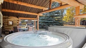 A hot tub under a wooden pergola with a log cabin backdrop. - Rendezvous Lodge (Red Lodge)
