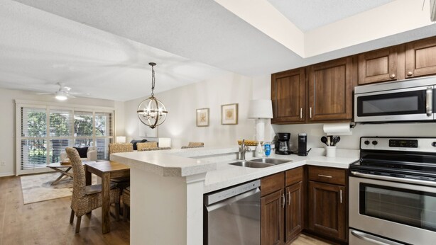A modern kitchen with wooden cabinets, stainless steel appliances, and a dining area with wicker chairs. - 307 Sailmaker in Summer Beach (Fernandina Beach)