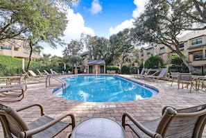 A swimming pool with lounge chairs and a table, surrounded by trees and buildings.